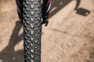 Close-up of a bicycle parked on a dirt trail, with a focus on the kickstand. The bike's rugged tires are well-suited for trail riding, and the scene suggests a forest environment. photo