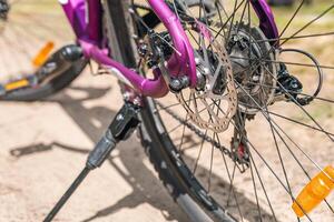 Close-up of a bicycle parked on a dirt trail, with a focus on the kickstand. The bike's rugged tires are well-suited for trail riding, and the scene suggests a forest environment. photo