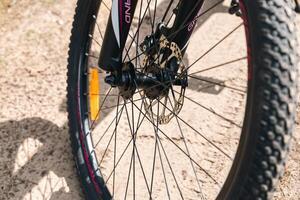 Close-up of a bicycle parked on a dirt trail, with a focus on the kickstand. The bike's rugged tires are well-suited for trail riding, and the scene suggests a forest environment. photo