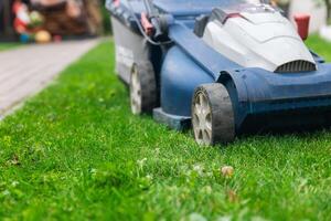 Person using a lawn mower to cut grass in a garden. The mower has a sturdy design with large wheels and is being pushed forward. In the background, there are some garden features. photo