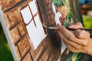 Close-up of someone skillfully painting on a canvas. The artwork looks like it depicts a rustic scene, possibly featuring elements like bricks or wood, giving it a cozy, homely feel. photo