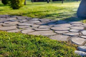 Beautiful garden path made of irregular, natural stones. The path winds through a lush, green lawn. The path is well-maintained, and the grass is trimmed evenly. Landscape design. photo