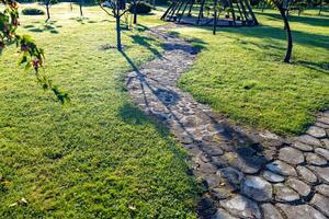 Well-maintained garden with a winding stone pathway leading to a small wooden bridge over a narrow stream. The pathway is made of irregularly shaped stones, adding a rustic charm to the scene. photo