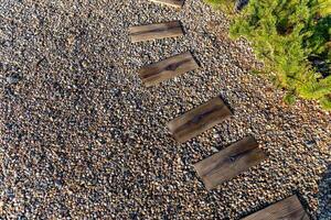 Pathway made of wooden planks placed on a bed of gravel. The wooden planks are arranged in a winding pattern, creating a natural and inviting walkway. The gravel surrounding the planks. photo