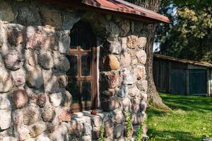 Rustic stone building with a charming window. The wall is built from irregularly shaped stones, adding to its natural and historical charm. The window, framed in dark wood. photo