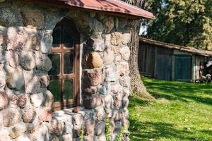 Rustic stone building with a charming window. The wall is built from irregularly shaped stones, adding to its natural and historical charm. The window, framed in dark wood. photo