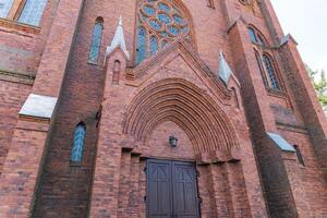 Gothic-style church, characterized by its pointed arches, tall spires, and intricate brickwork. The architecture includes large stained glass windows, likely with elaborate designs. photo