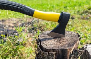 A small, rather heavy ax stuck in a stump for chopping wood. Close-up photograph of an axe stuck in a wooden tree stump, illustrating themes of nature, the outdoors, and woodworking. photo