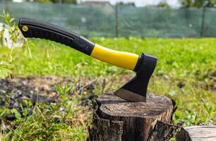 A small, rather heavy ax stuck in a stump for chopping wood. Close-up photograph of an axe stuck in a wooden tree stump, illustrating themes of nature, the outdoors, and woodworking. photo