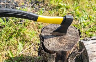 A small, rather heavy ax stuck in a stump for chopping wood. Close-up photograph of an axe stuck in a wooden tree stump, illustrating themes of nature, the outdoors, and woodworking. photo