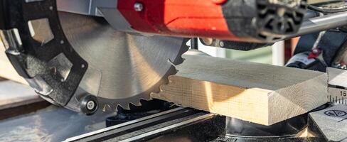 Miter saw tool blade up close for cutting lumber and carpentry. Using a circular saw to cut a wooden board. Blade of a miter saw to cut off the edge of a wooden board, close up. photo