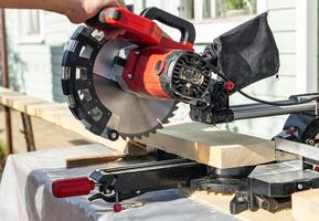 Cuts a wooden beam using a circular saw. Home furniture workshop. Work in his carpentry workshop. Miter saw and planks for building a house. photo
