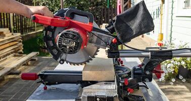 Cuts a wooden beam using a circular saw. Home furniture workshop. Work in his carpentry workshop. Miter saw and planks for building a house. photo