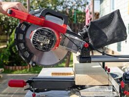 Cuts a wooden beam using a circular saw. Home furniture workshop. Work in his carpentry workshop. Miter saw and planks for building a house. photo