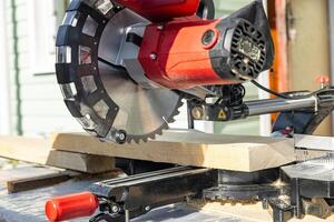 Cuts a wooden beam using a circular saw. Home furniture workshop. Work in his carpentry workshop. Miter saw and planks for building a house. photo