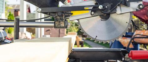 Cuts a wooden beam using a circular saw. Home furniture workshop. Work in his carpentry workshop. Miter saw and planks for building a house. photo