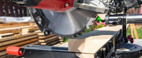 Cuts a wooden beam using a circular saw. Home furniture workshop. Work in his carpentry workshop. Miter saw and planks for building a house. photo