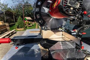 Using a miter saw to cut a piece of wood. Own carpentry workshop. Sawing a wooden board with a miter saw. Safe equipment for the furniture and construction industry. Close-up. photo