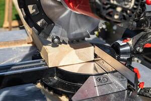 Using a miter saw to cut a piece of wood. Own carpentry workshop. Sawing a wooden board with a miter saw. Safe equipment for the furniture and construction industry. Close-up. photo