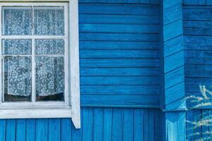 Close-up of a wooden building with windows. The building is painted in a bright, vibrant blue. The windows are framed in white, providing a stark contrast to the blue background. photo