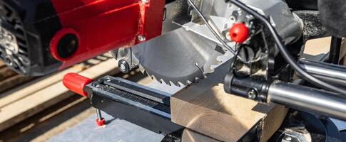 Cuts a wooden beam using a circular saw. Home furniture workshop. Work in his carpentry workshop. Miter saw and planks for building a house. photo