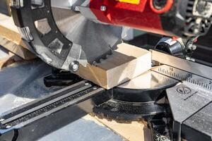 Using a miter saw to cut a piece of wood. Own carpentry workshop. Sawing a wooden board with a miter saw. Safe equipment for the furniture and construction industry. Close-up. photo
