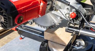 Cuts a wooden beam using a circular saw. Home furniture workshop. Work in his carpentry workshop. Miter saw and planks for building a house. photo