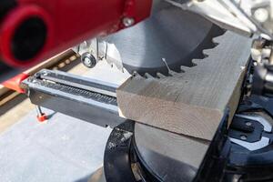 Using a miter saw to cut a piece of wood. Own carpentry workshop. Sawing a wooden board with a miter saw. Safe equipment for the furniture and construction industry. Close-up. photo