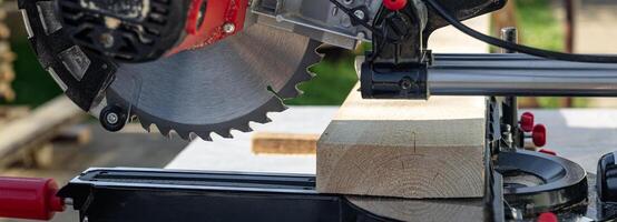 Cuts a wooden beam using a circular saw. Home furniture workshop. Work in his carpentry workshop. Miter saw and planks for building a house. photo