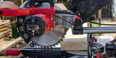 Cuts a wooden beam using a circular saw. Home furniture workshop. Work in his carpentry workshop. Miter saw and planks for building a house. photo