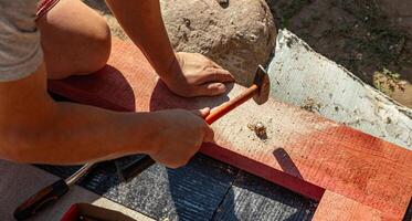 A person skillfully positions a nail against a piece of wood, preparing for a precise hammering technique. The focus is on the careful alignment needed for effective and accurate nailing as they bring photo