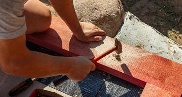 A person skillfully positions a nail against a piece of wood, preparing for a precise hammering technique. The focus is on the careful alignment needed for effective and accurate nailing as they bring photo