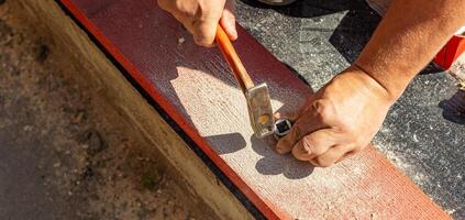 A person skillfully positions a nail against a piece of wood, preparing for a precise hammering technique. The focus is on the careful alignment needed for effective and accurate nailing as they bring photo