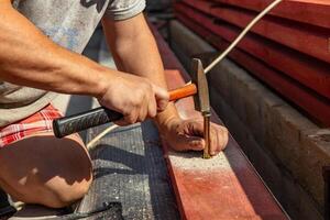 A person skillfully positions a nail against a piece of wood, preparing for a precise hammering technique. The focus is on the careful alignment needed for effective and accurate nailing as they bring photo