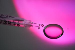 Injection syringe with a drop of drug on a rich pink background. photo