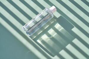 Bottle of facial toner or cleanser on a green background with stripes shadows. photo