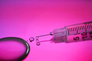 Injection syringe with a drop of drug on a rich pink background. photo