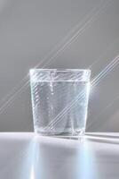 Glass of clean filtered water on white background with beautiful glare. photo