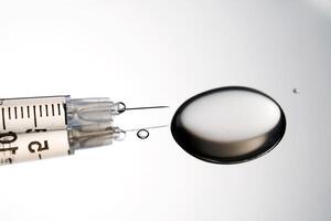 Injection syringe with a drop of drug on a stainless steel background. photo