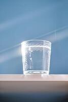 Glass of clean filtered water on blue background with beautiful glare. photo