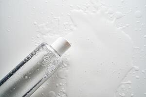 Bottle of facial toner or cleanser on white background with drops of product. photo