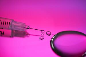 Injection syringe with a drop of drug on a rich pink background. photo