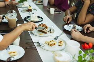 Woman hand cutting slice of cake cake with group of friends meeting at cafe. photo