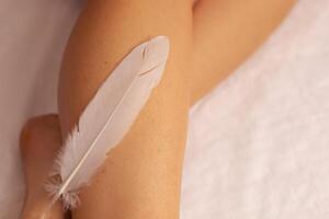 A person gently touches a soft feather against their leg in a serene indoor setting photo