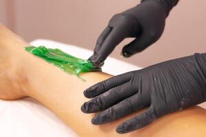 Aesthetician performing a green wax treatment on a clients leg in a spa setting photo