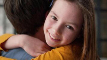 Positive Caucasian family little girl embracing dad male father parent cuddling hug at home happy child smiling with healthy white teeth daughter looking at camera parent guy man kid enjoying weekend video