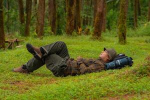 Asian adventurers enjoy the serenity of the wild by resting on the green grass in the pine forest area. A male adventurer was lying on the green grass in a quiet pine forest area. photo