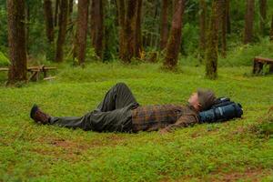 Asian adventurers enjoy the serenity of the wild by resting on the green grass in the pine forest area. A male adventurer was lying on the green grass in a quiet pine forest area. photo