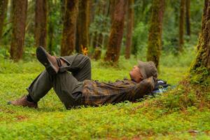 Asian adventurers enjoy the serenity of the wild by resting on the green grass in the pine forest area. A male adventurer was lying on the green grass in a quiet pine forest area. photo