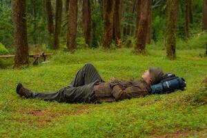 Asian adventurers enjoy the serenity of the wild by resting on the green grass in the pine forest area. A male adventurer was lying on the green grass in a quiet pine forest area. photo